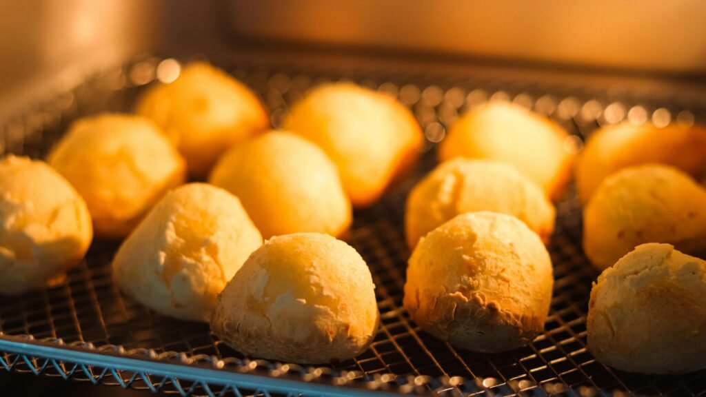 pexels-photo-20450299-20450299 Freshly baked cheese bread rolls on a rack with warm lighting in the oven.